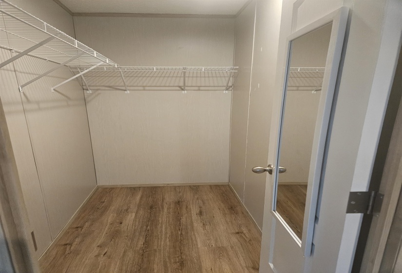 Walk-in closet featuring wood-finish flooring, white wire shelving, and a white door with an integrated full-length mirror