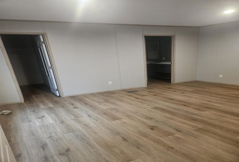 Spacious room featuring wood-finish flooring and light gray paneled walls