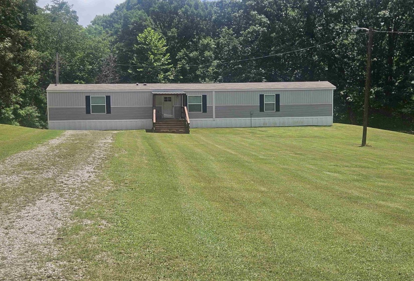 Manufactured home featuring two-tone siding, dark window shutters, a front entry with wooden steps, and an awning over the entry