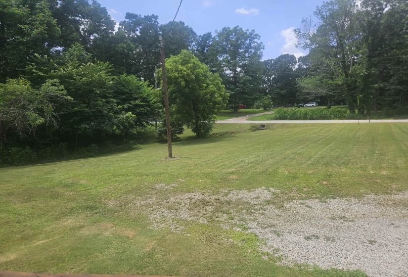 Expansive outdoor space featuring a large grassy lawn, gravel area, and mature trees bordering the property