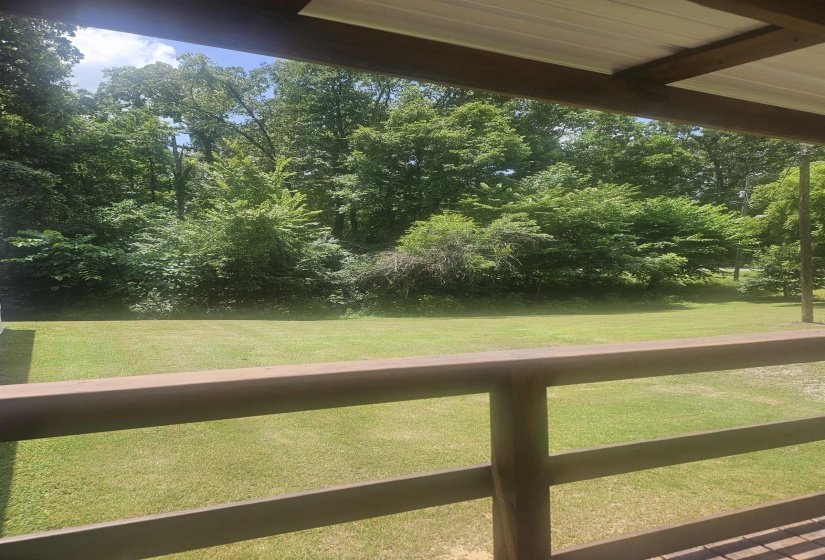Expansive green lawn framed by mature trees, visible from a covered outdoor area with a durable metal roof and sturdy wooden railings