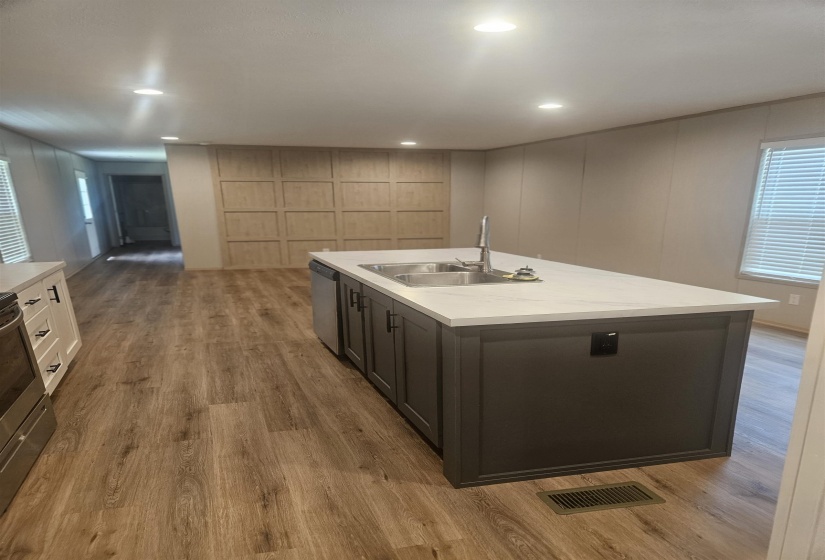 Spacious kitchen featuring a large island with a double basin sink, light-toned countertops, dark cabinetry, and wood-finish flooring