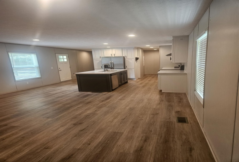 Open-concept kitchen and living area featuring wood-finish flooring, recessed lighting, a kitchen island with sink, white cabinetry, and stainless steel appliances