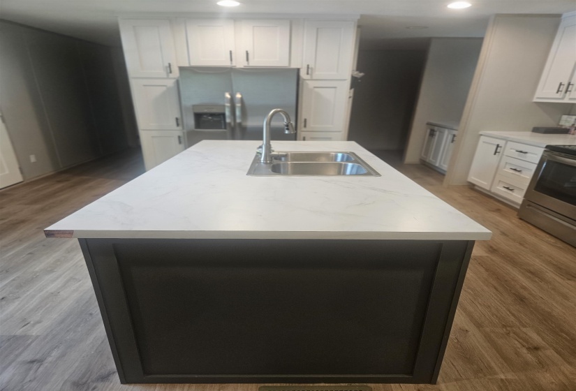 Kitchen island featuring a double basin stainless steel sink with a gooseneck faucet, light-toned countertop, and dark-toned cabinetry