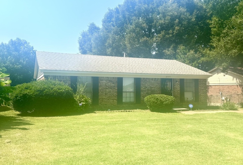 Brick facade home with a gray shingle roof, dark shutters, and a covered entry