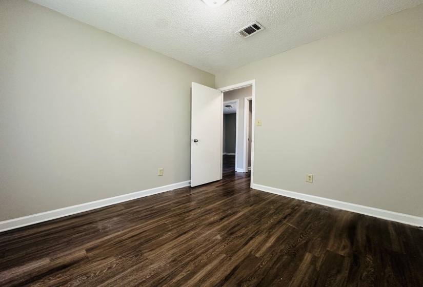 Spacious room featuring wood-finish flooring, light neutral wall paint, and crisp white baseboards