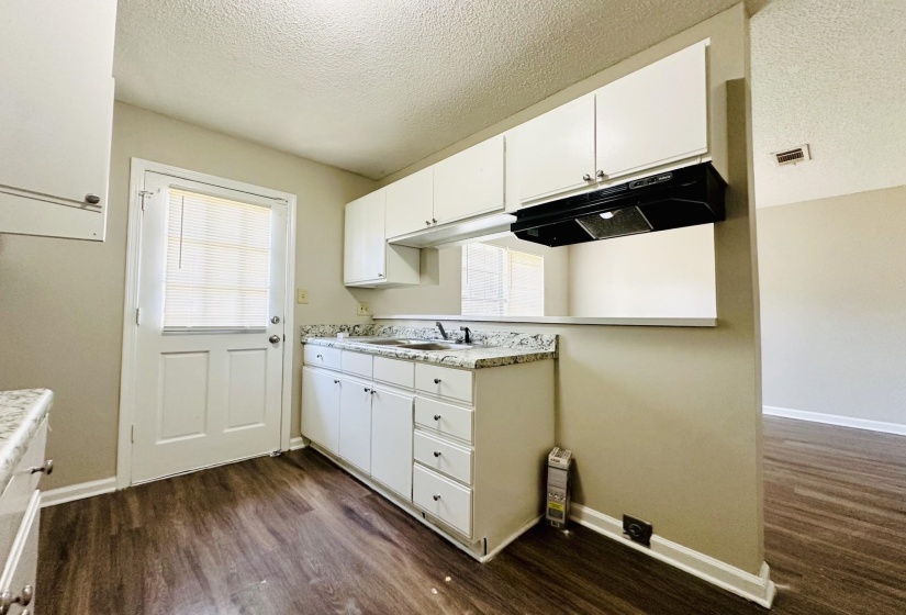 Kitchen featuring white cabinetry, light-colored countertops, a single basin sink, a black range hood, and wood-finish flooring
