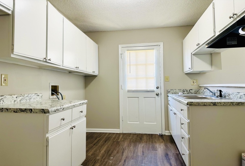 Utility room featuring white cabinetry, wood-finish flooring, and a door with integrated blinds