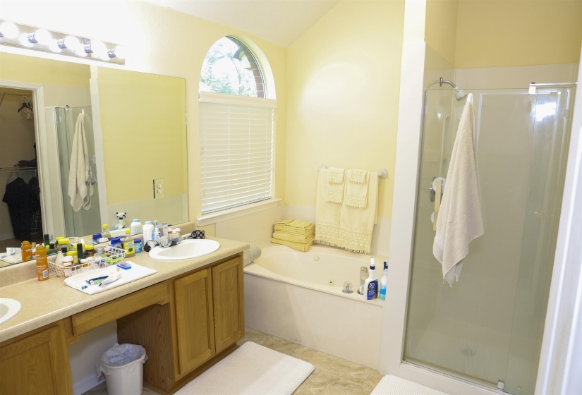 Bathroom featuring a double vanity with wood-finish cabinetry, a drop-in tub, a separate shower enclosure, and an arched window with blinds