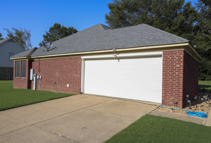 Brick exterior with a gray asphalt shingle roof, integrated garage, concrete driveway, and established lawn