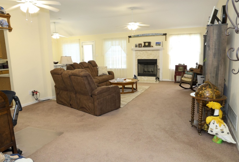 Spacious living area featuring neutral carpeting, a tiled fireplace with mantel, and multiple large windows