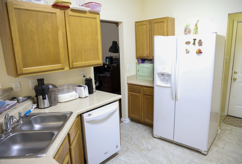 Kitchen featuring light wood cabinetry, a double basin stainless steel sink, a white dishwasher, a side-by-side refrigerator with an ice and water dispenser, and neutral-toned tile flooring