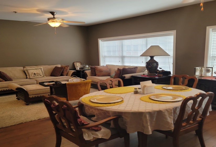 Open-concept living and dining area featuring wood-finish flooring, neutral wall tones, and multiple windows with blinds