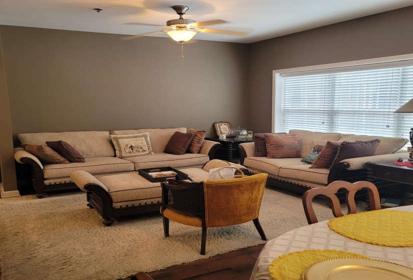 Living area featuring a ceiling fan with integrated lighting, a large window with blinds, and wood-finish flooring