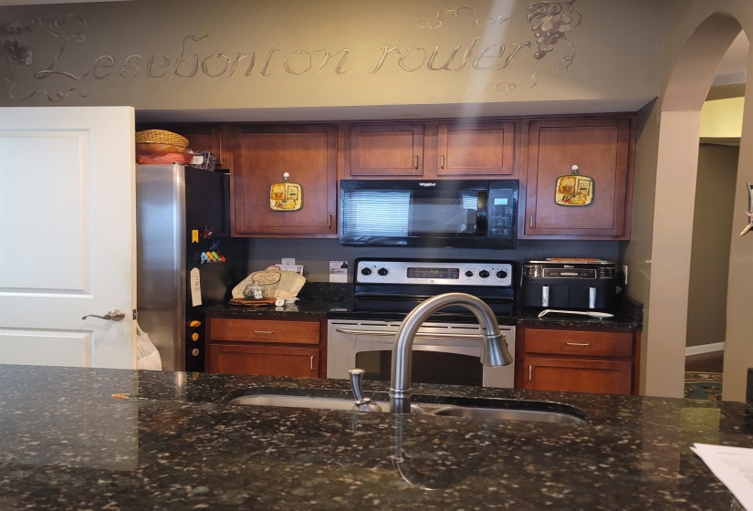 Kitchen featuring dark wood cabinetry, a stainless steel electric range, an over-range microwave, and dark speckled countertops with an undermount sink and gooseneck faucet