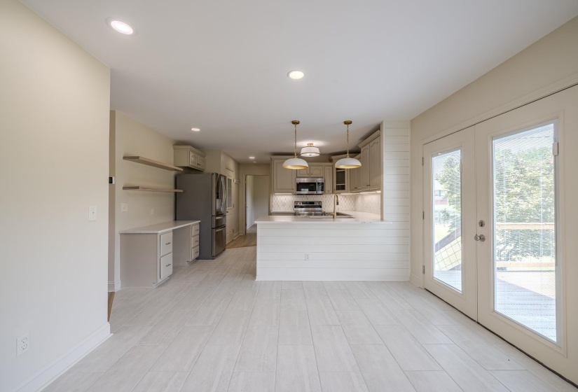 Open-concept kitchen and dining area featuring light wood-finish flooring, a kitchen island with shiplap detail, recessed lighting, double French doors, and stainless steel appliances