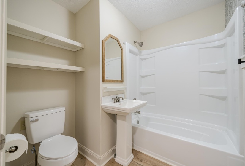 Bathroom featuring a white pedestal sink, toilet, and bathtub with integrated shelving