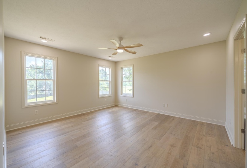 Spacious room featuring wood-finish flooring, light-toned walls, and multiple double-hung windows