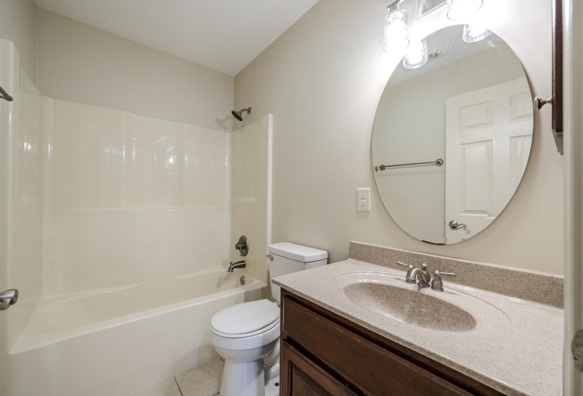Bathroom featuring a vanity with a speckled countertop, undermount sink, and a circular mirror