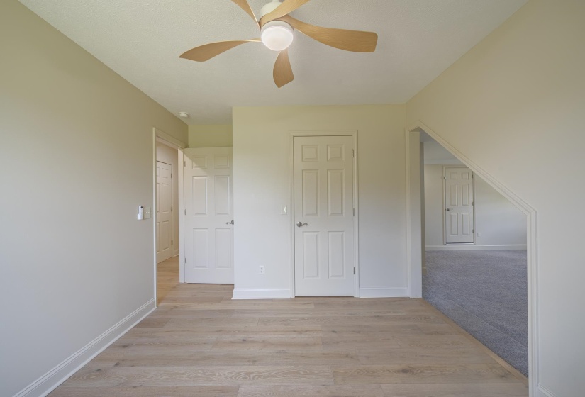 Spacious room with wood-finish flooring, light neutral wall tones, and a contemporary ceiling fan with integrated lighting