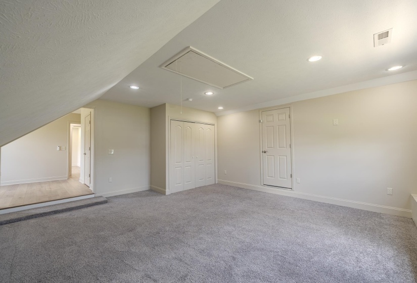 Spacious room featuring light gray carpeting, recessed lighting, white trim, a closet with bi-fold doors, and a paneled door