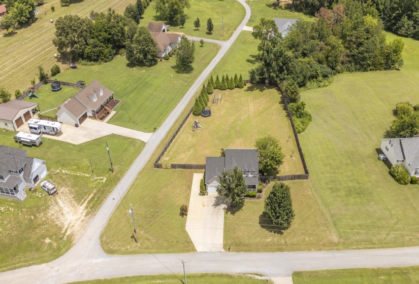 Aerial view showcasing a property with a paved driveway, mature trees, and a spacious green lawn