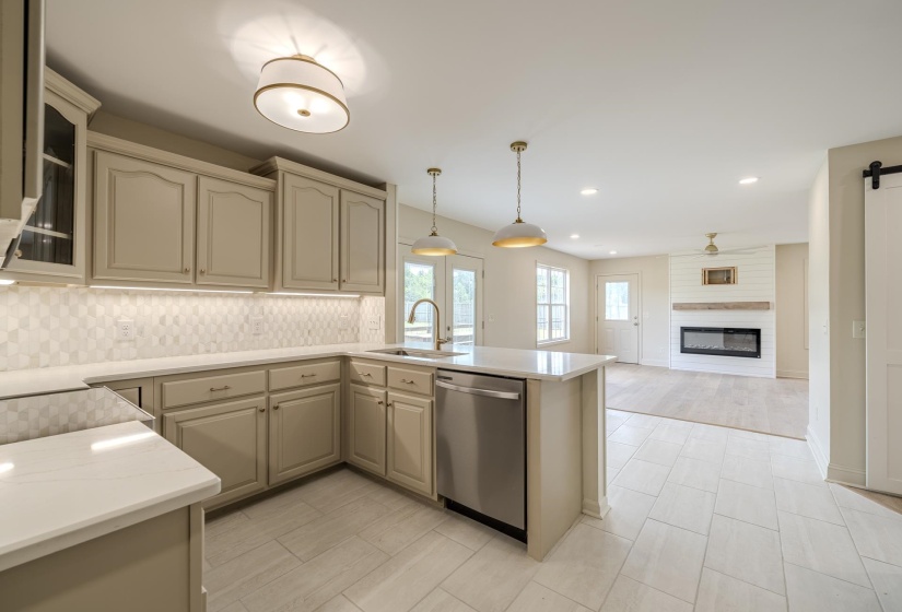Modern kitchen featuring light-toned cabinetry, quartz countertops, stainless steel appliances, and a patterned tile backsplash