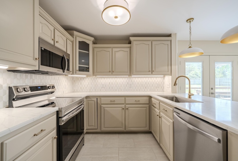Well-appointed kitchen featuring light-toned cabinetry, quartz countertops, a geometric tile backsplash, and stainless steel appliances