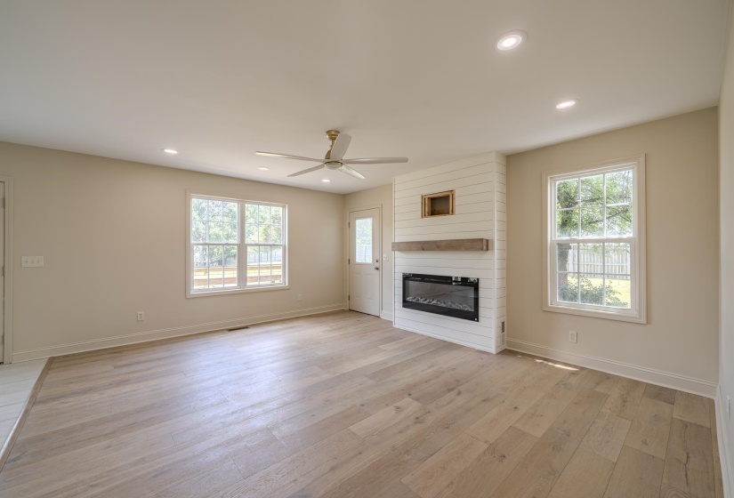 Spacious living area featuring wood-finish flooring, a shiplap fireplace with a wood mantle and electric insert, and recessed lighting
