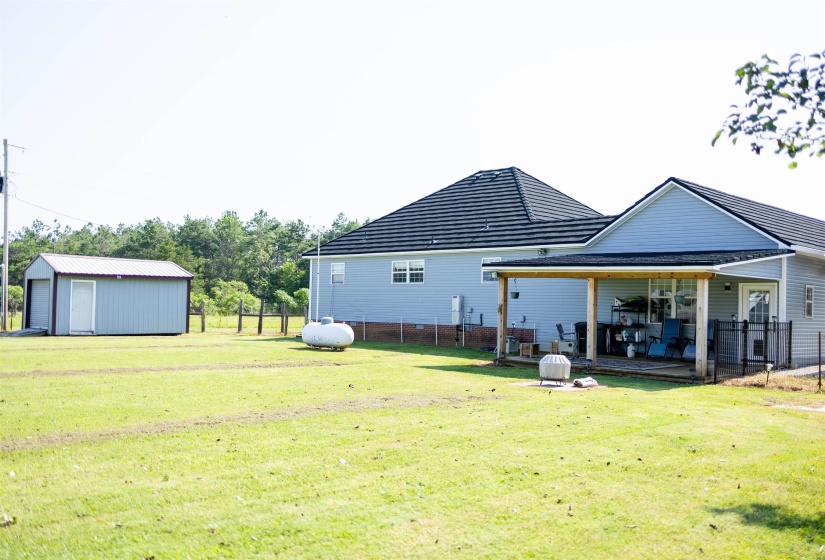 Expansive backyard featuring a covered patio, a detached storage shed with a roll-up door, light blue siding, and a dark tile roof