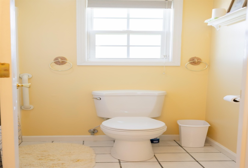 Bathroom featuring a white toilet, white grid-patterned floor tiles, and a window with white trim
