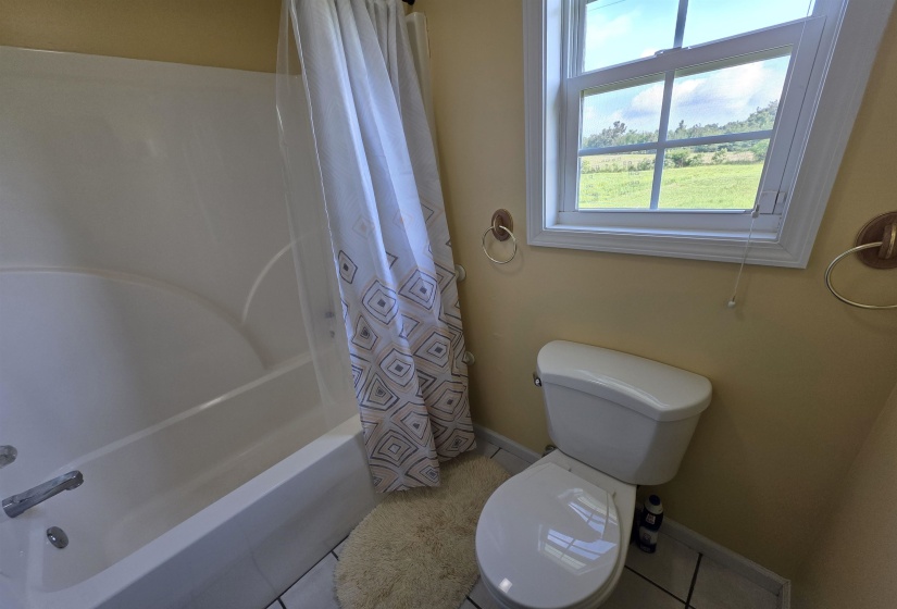 White ceramic tub and shower combination with chrome fixtures, a white toilet, and a framed window