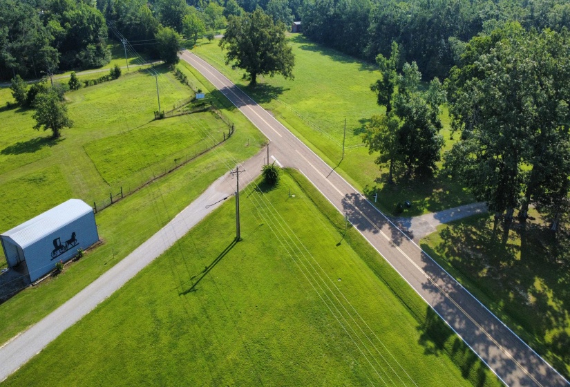 Expansive green landscape featuring a paved road, mature trees, a metal storage building, and fencing