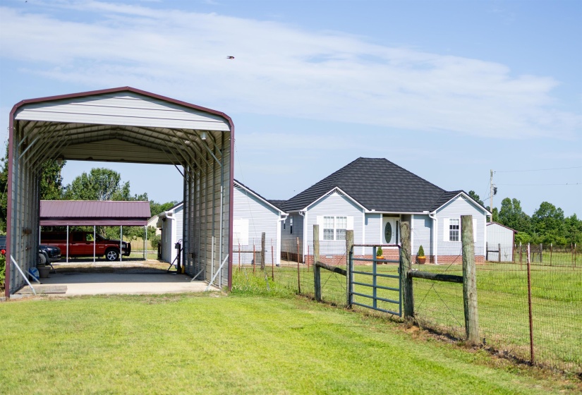 Expansive property featuring a light blue exterior residence with a dark shingle roof, a large metal carport, and a second covered parking structure