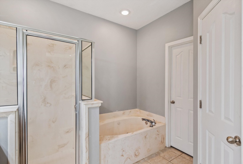 Shower enclosure with framed glass door, corner soaking tub, and tile flooring