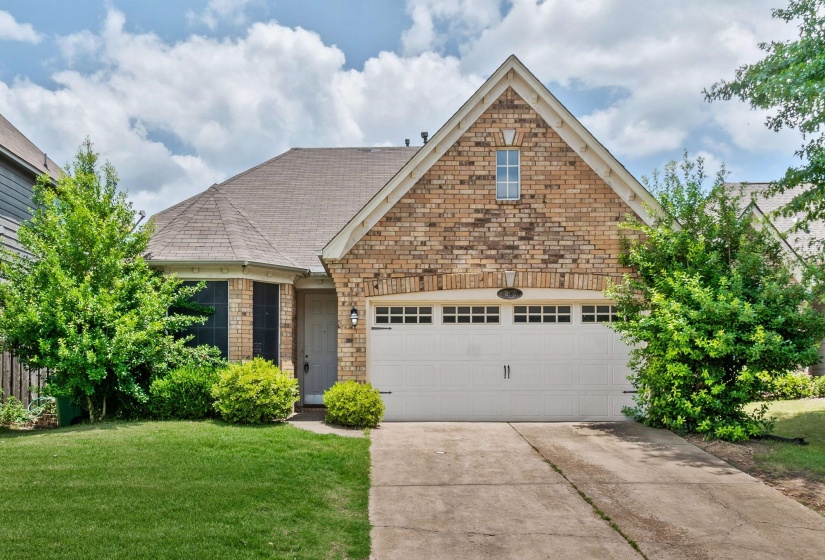 Brick facade residence featuring a front-facing garage with a paneled door, a gabled roofline, and a bay window