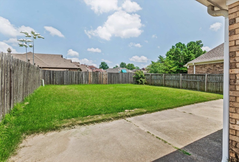 Expansive rear yard featuring a concrete patio, grassy lawn, and full wood privacy fencing