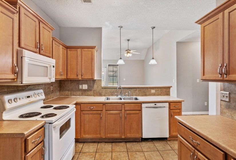 Kitchen featuring wood cabinetry, laminate countertops, tile flooring, and integrated white appliances including a range, microwave, and dishwasher