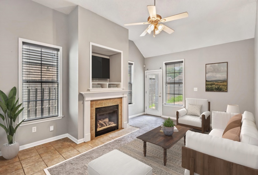Living area featuring a gas fireplace with a tiled surround and white mantle, vaulted ceilings, and a ceiling fan