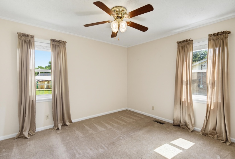 Interior room featuring two windows with natural light, a ceiling fan with integrated lighting, crown molding, and neutral-toned carpeting