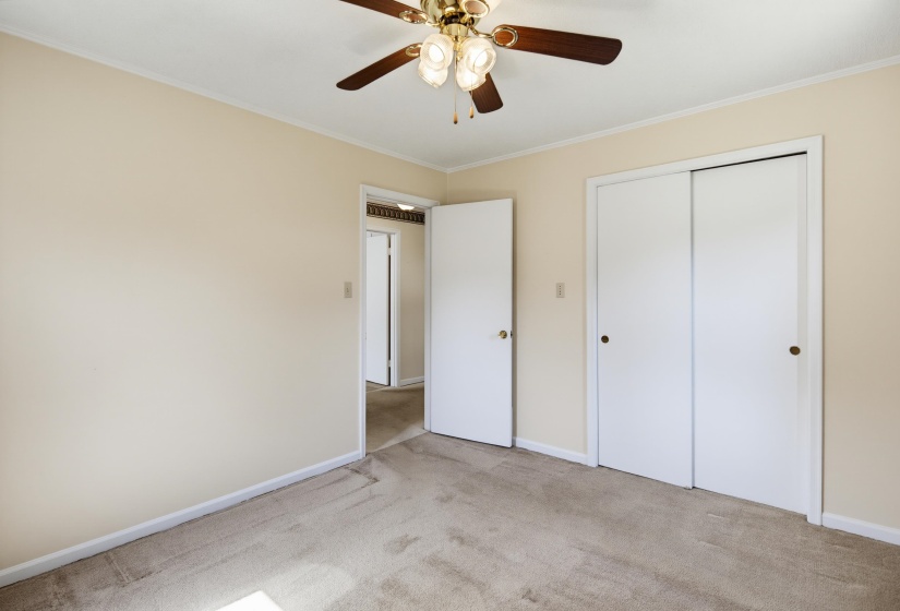Carpeted room featuring a ceiling fan with light fixture, neutral wall paint, white trim, and bi-fold closet doors