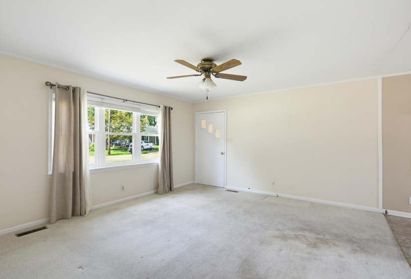 Spacious interior room featuring light-colored carpet flooring, a large multi-pane window, and a ceiling fan with light fixture
