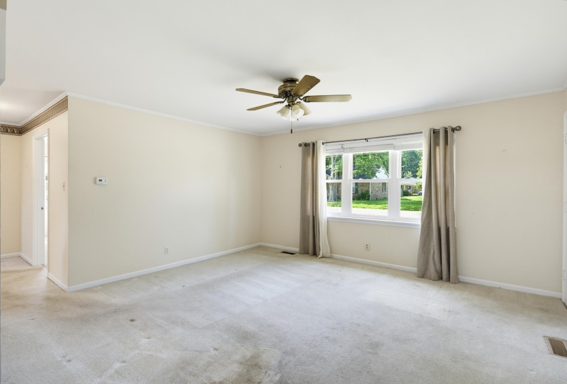 Spacious room featuring neutral-toned walls, a large multi-pane window, and a ceiling fan with light fixture