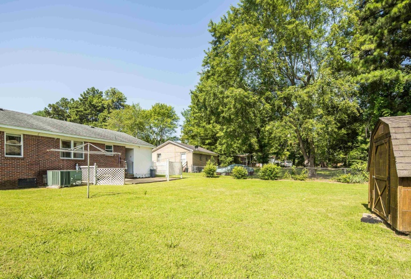 Expansive green lawn featuring mature trees, a detached storage shed, and a brick exterior home with a white lattice-enclosed patio