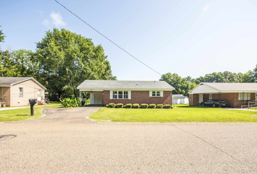 Brick ranch-style home featuring a covered carport, established landscaping, and a paved driveway