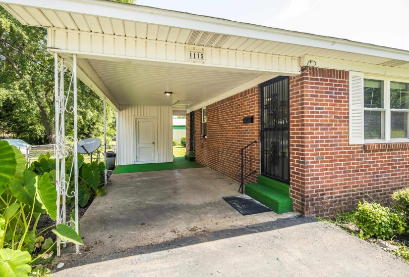 Brick exterior featuring a covered carport with decorative metal supports, an exterior storage room, and a front entry with a security screen door and handrail