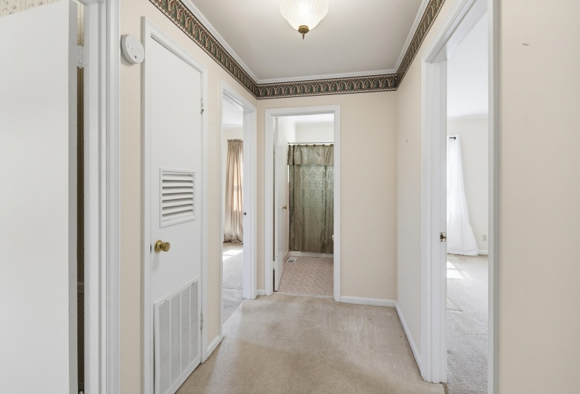 Carpeted hallway featuring multiple doorways, a ceiling-mounted light fixture, and crown molding with a decorative border