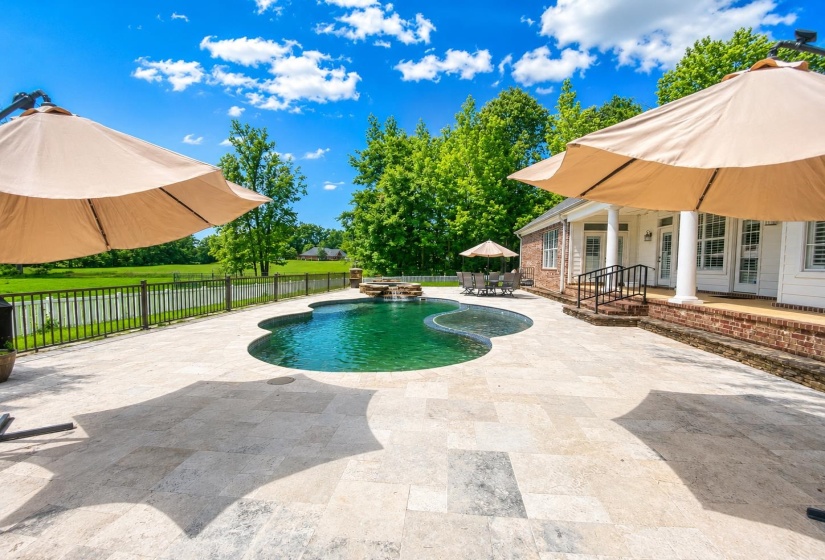Freeform swimming pool with a stone waterfall feature, surrounded by an expansive stone patio