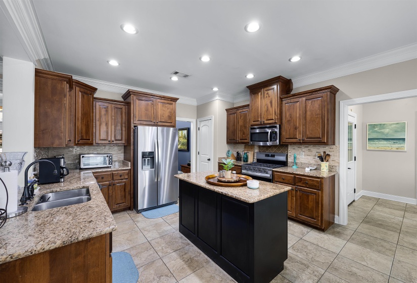 Kitchen with stainless steel appliances, light stone counters, crown molding, a center island, and recessed lighting