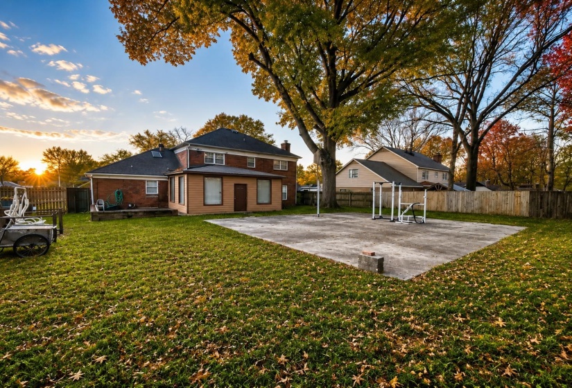 Expansive backyard featuring a large concrete pad, mature trees, and a wooden fence boundary